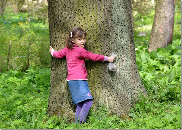 The little girl embraces a trunk of a big tree